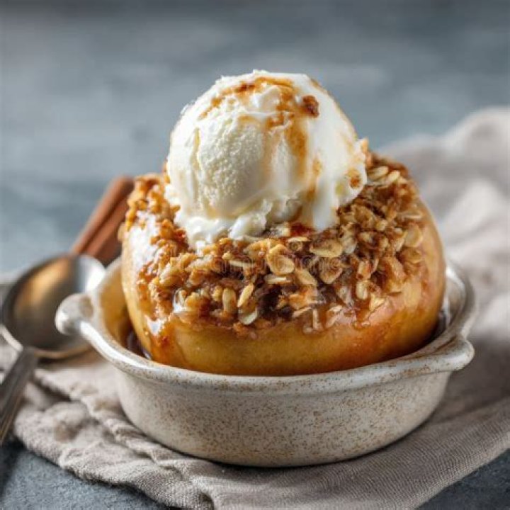 Baked apple topped with ice cream and caramel sauce on a white plate.