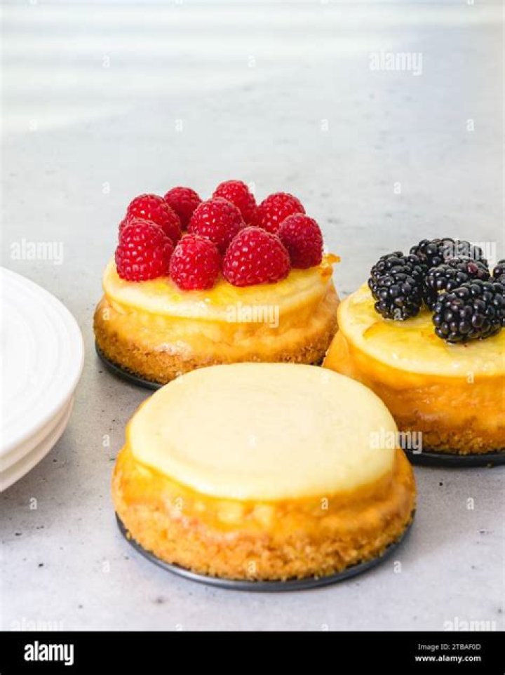 Mini cheesecakes on a grey plate topped with berries and whipped cream.
